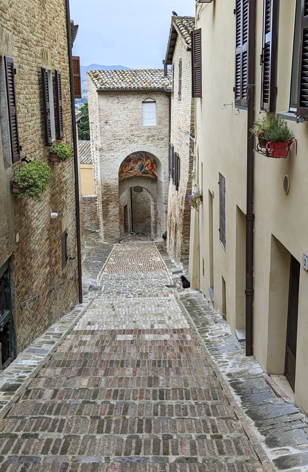 Narrow brick road leading to Porta Della Croce, with a black cat barely visible in the middle of the photo