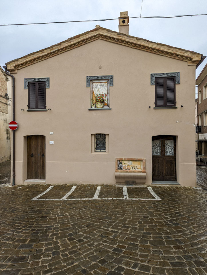 A wall with a spot painted like an open window with a plant, and below is a bench that looks like it has cats on it