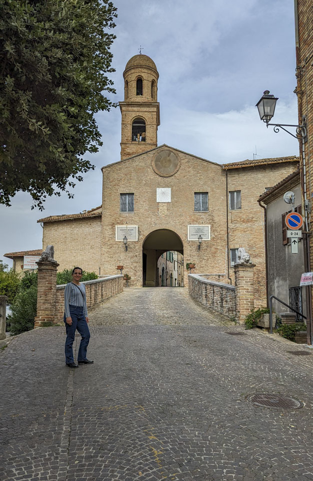 Anne in front of the entrance to Orciano, with the bell tower visible over the entryway.