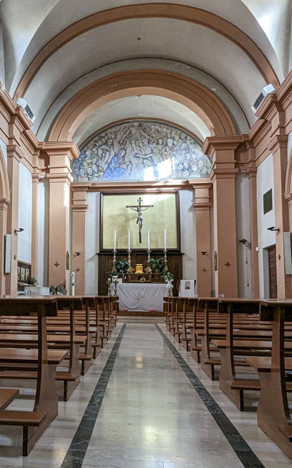 The aisle in the church, with the altar and cross at the end. The walls are peach and white.