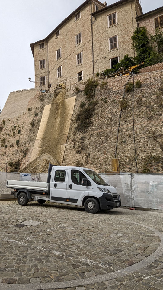 A pickup truck in front of a wall section being repaired. There are large pieces of plywood against the wall as protection for the wall when they send material cascading down the wall.