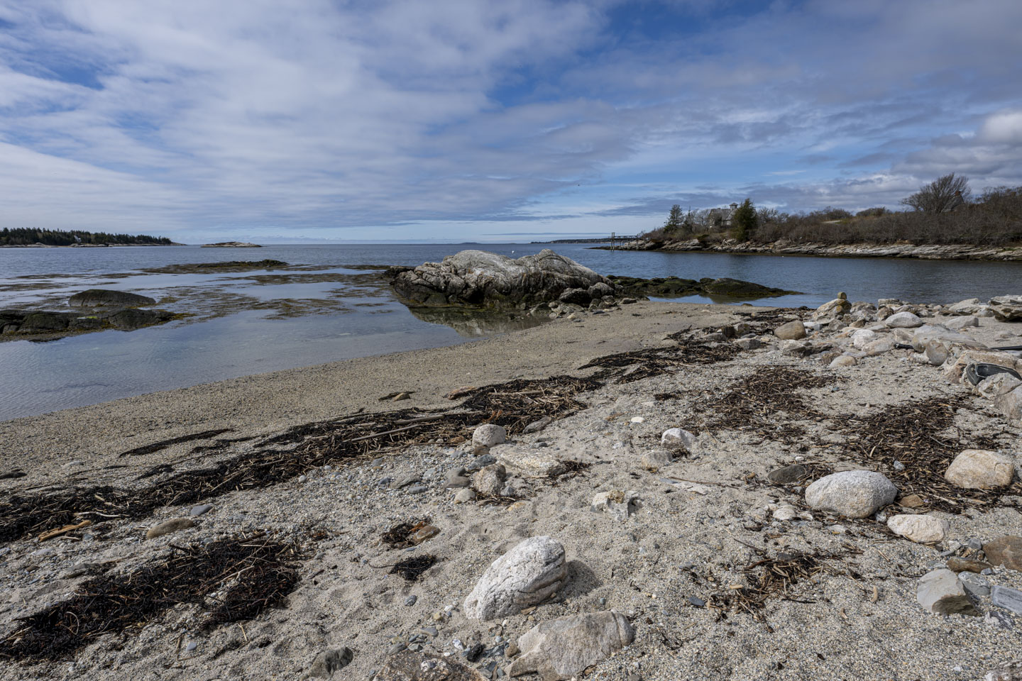 A beach that has many large rocks in it. The tide is out, and wet sand can be seen near the water. 