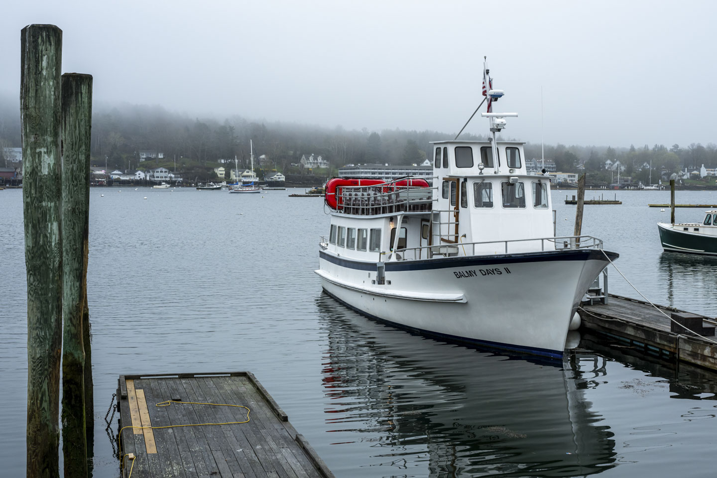 A boat named Balmy Days II is moored at a pier. It is a tour boat with seats at the top level as well as within a cabin.