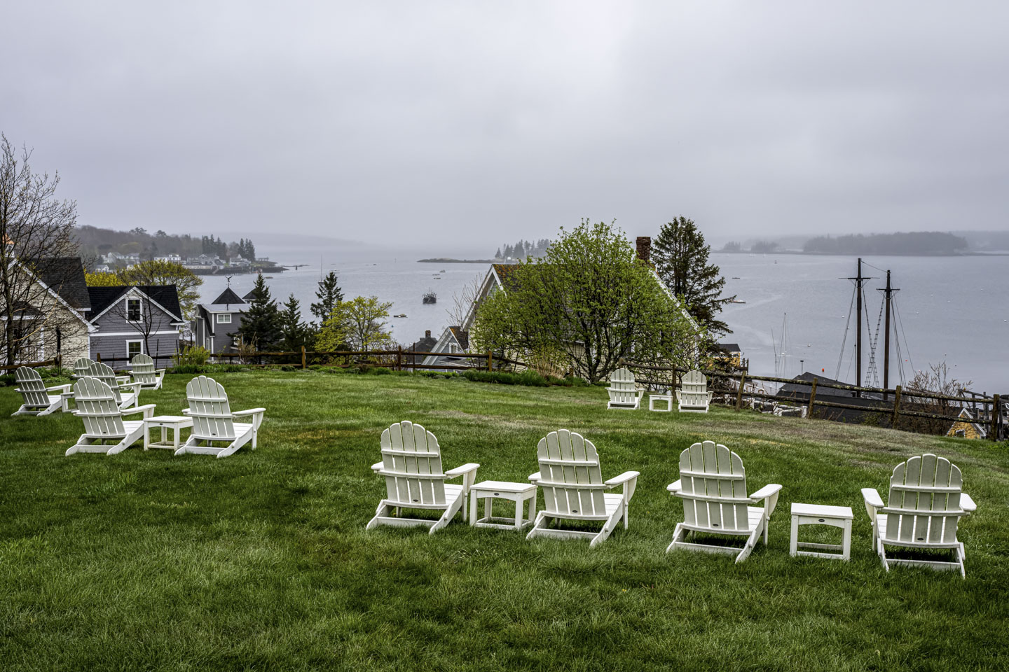 Standing on a green lawn that has white chairs, the harbor can se seen past some houses that are lower on the hill.  There is a bit of fog above the islands. 