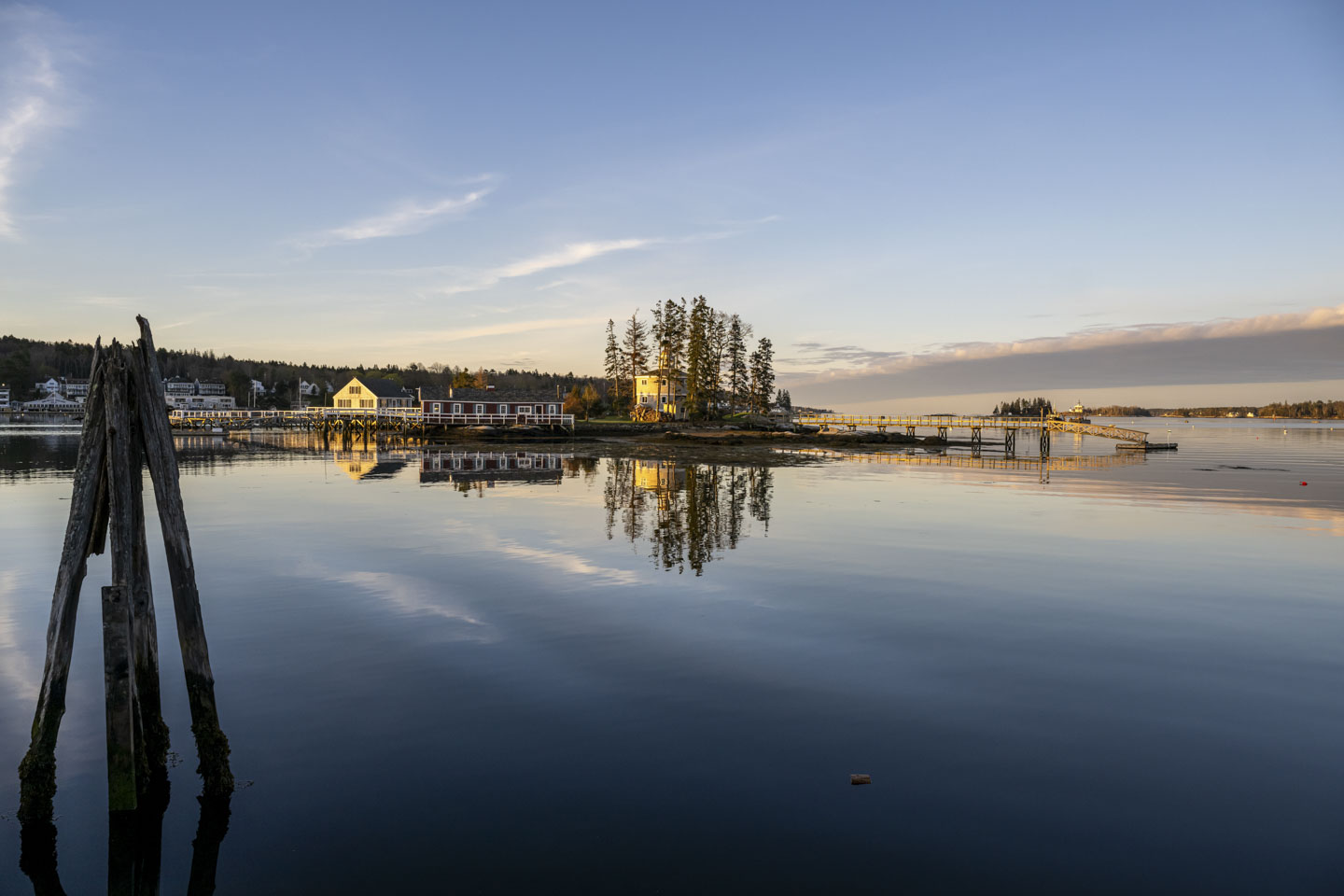 View over water to a round building surrounded by trees and a pier. Early morning sun gives the building a yellow glow.
