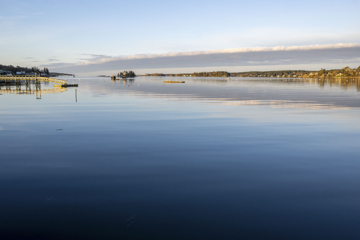 Relatively calm blue water leading out into the harbor, with the early morning sun shining on a pier on the left.