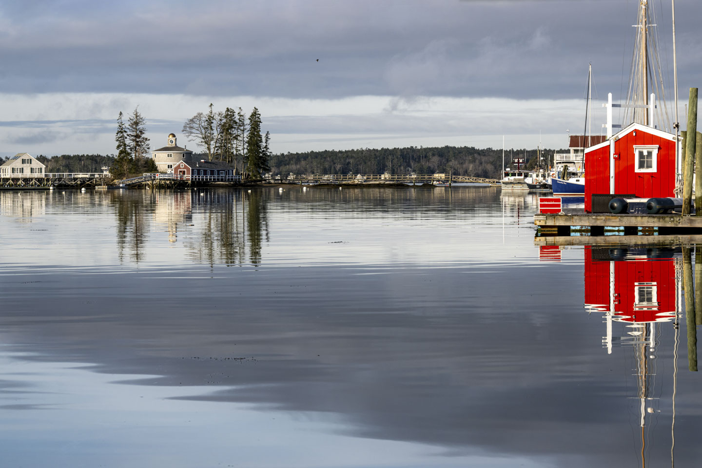 A brightly painted red shed sits on a pier on the right. On the left can be seen some land with 3 buildings on it.