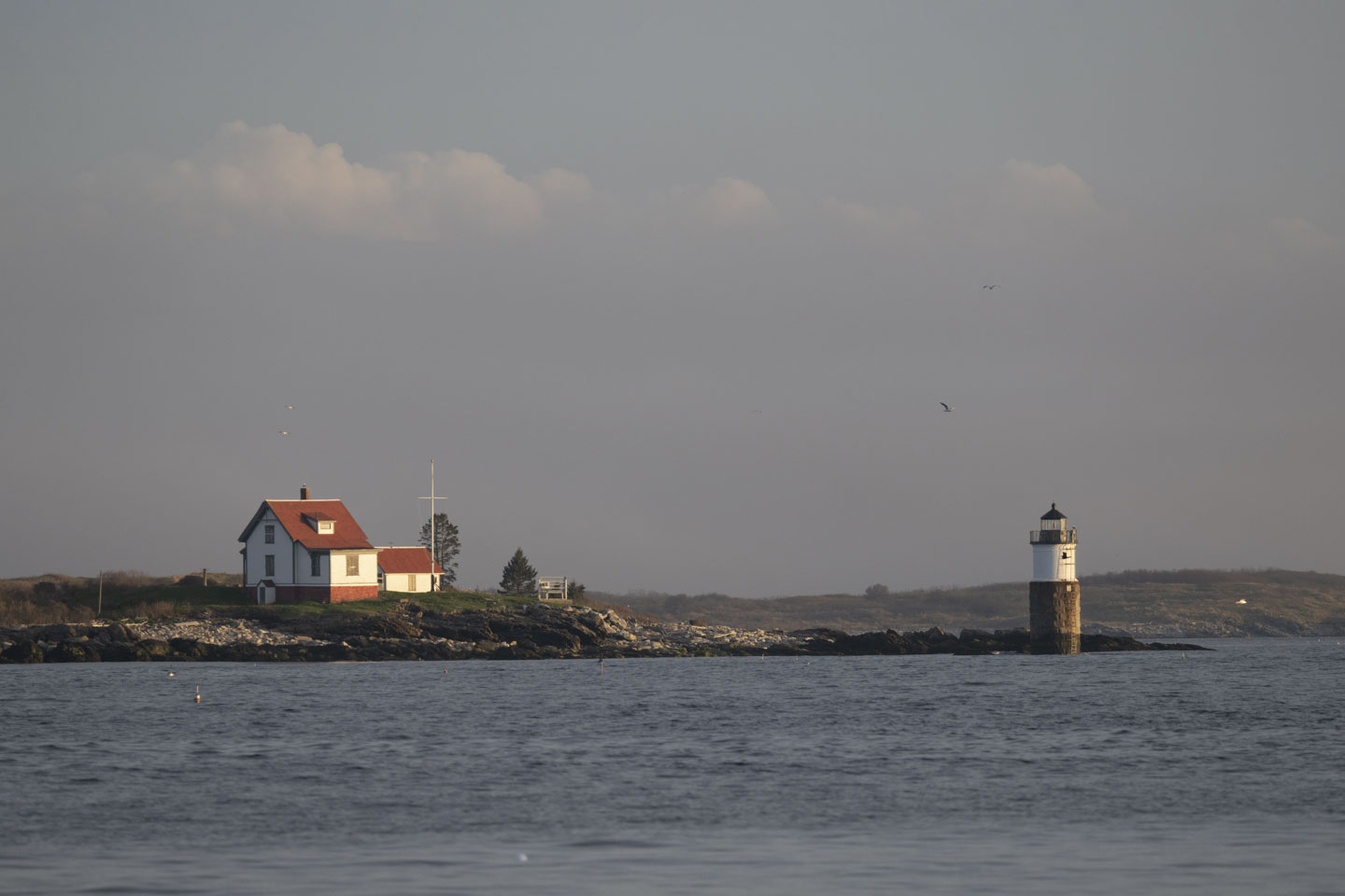 A close view of a light tower on the right with the associated house on the left. Water is in the foreground.