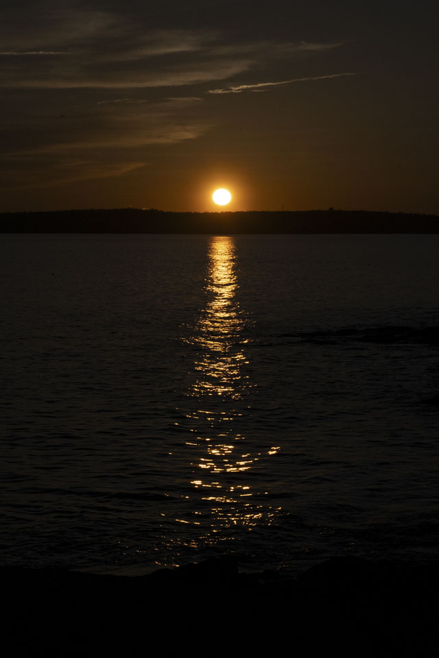 The sun is just above the horizon, causing a trail of light on the water. 