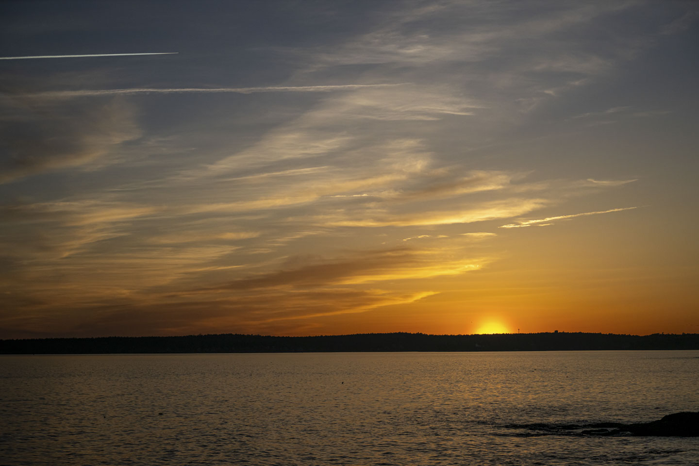The sun is mostly behind the horizon and is casting a lovely glow on the water and the sky.