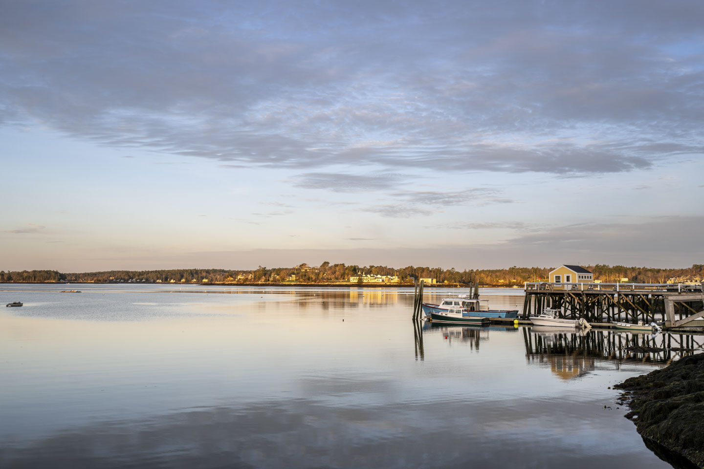 Sunrise shining on the opposite side of the water. Closer is a pier with some boats in the water.