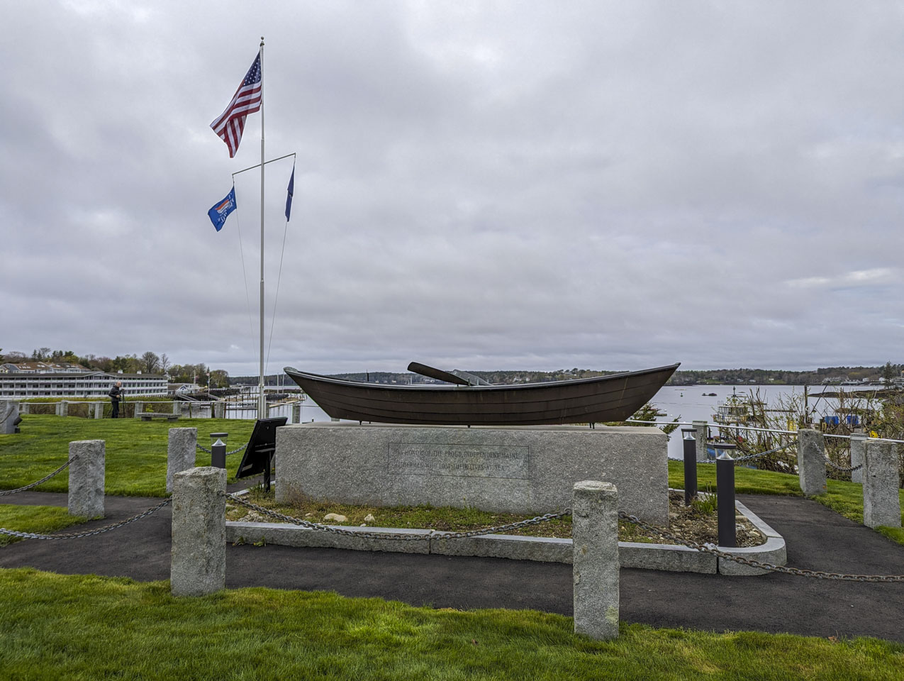 A grassy area with a monument. The monument is a skiff style boat on a solid granite base.