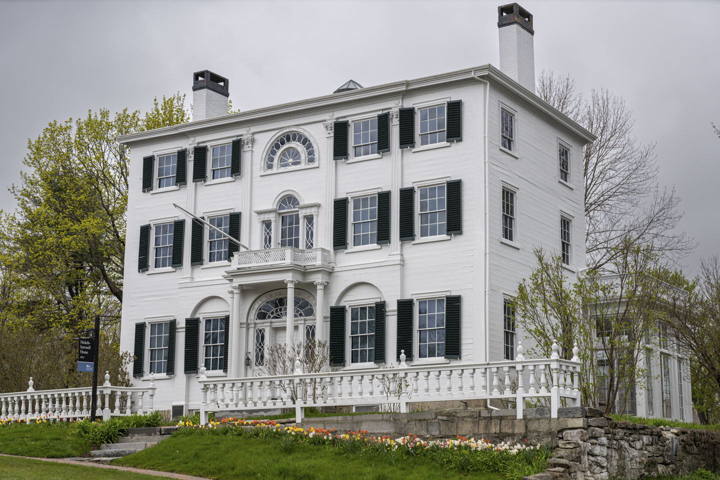 A stately 3-story white building has a historic marker sign in front of it.
