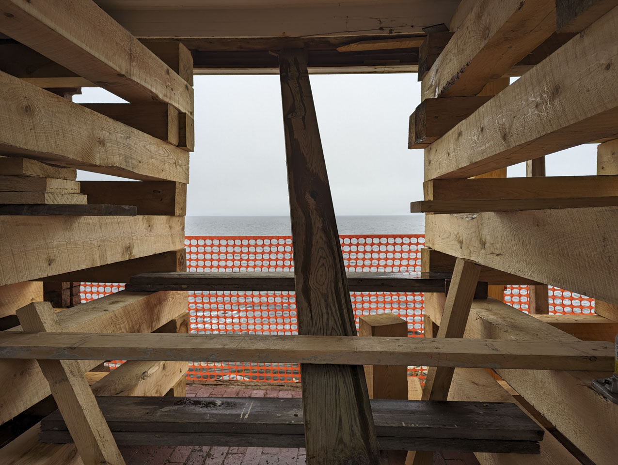 We are looking through the brick building where large wood beams are stacked on each side, supporting the roof.
