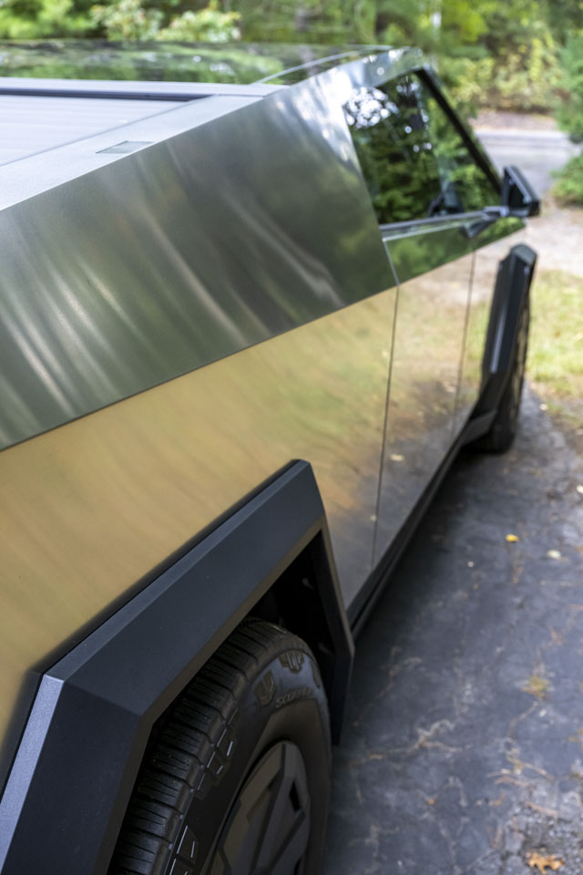Looking at the side of the Cybertruck with indistinct reflections of grass, dirt, and trees.