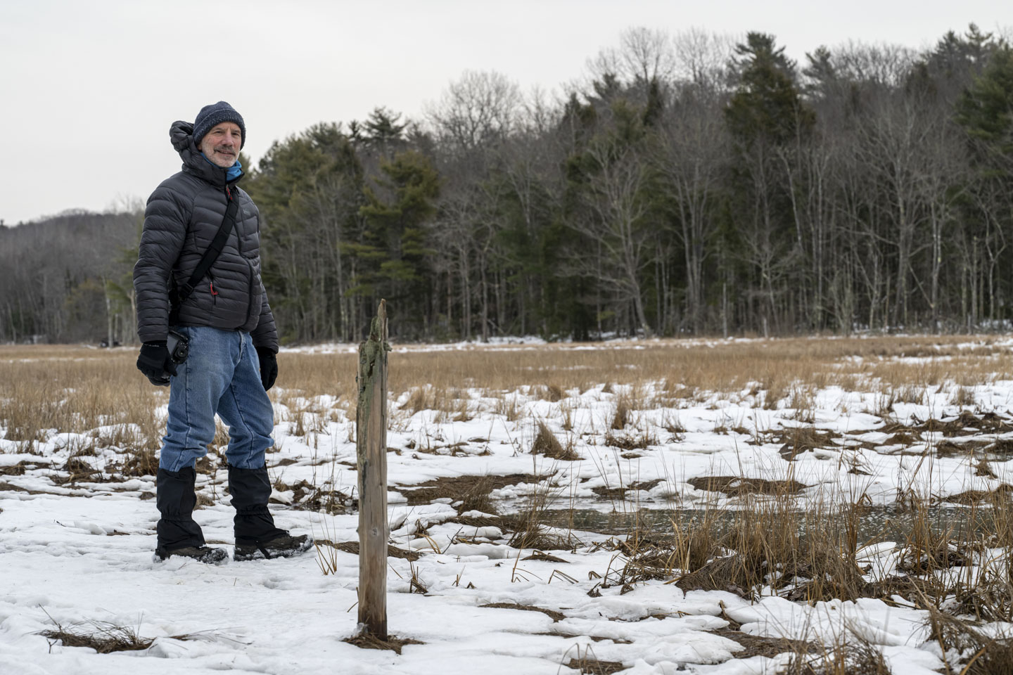 Paul is standing on snow in the marsh, and there is the stump of a small tree.