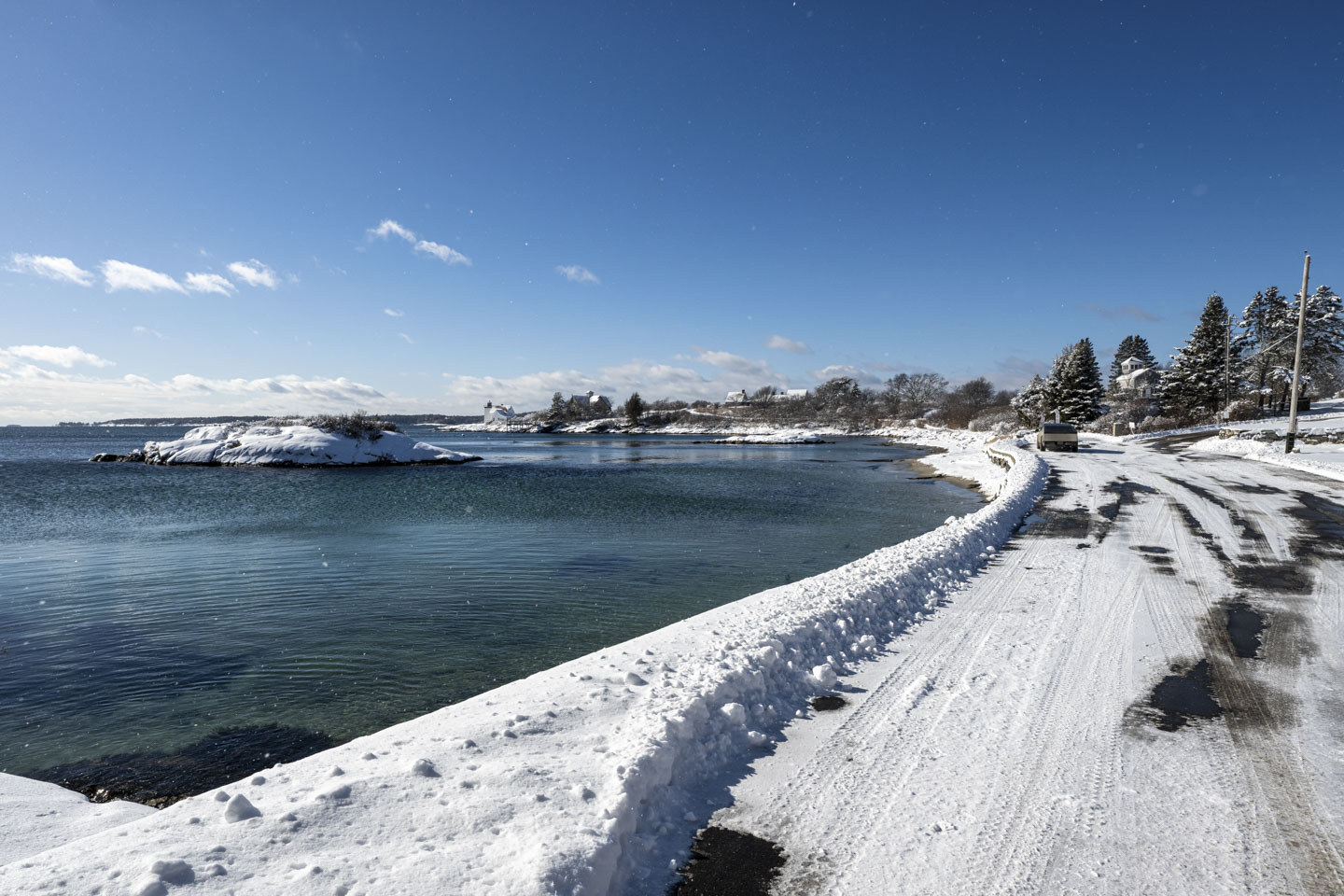 An intense blue sky is above a small harbor and a road that is covered with snow. 