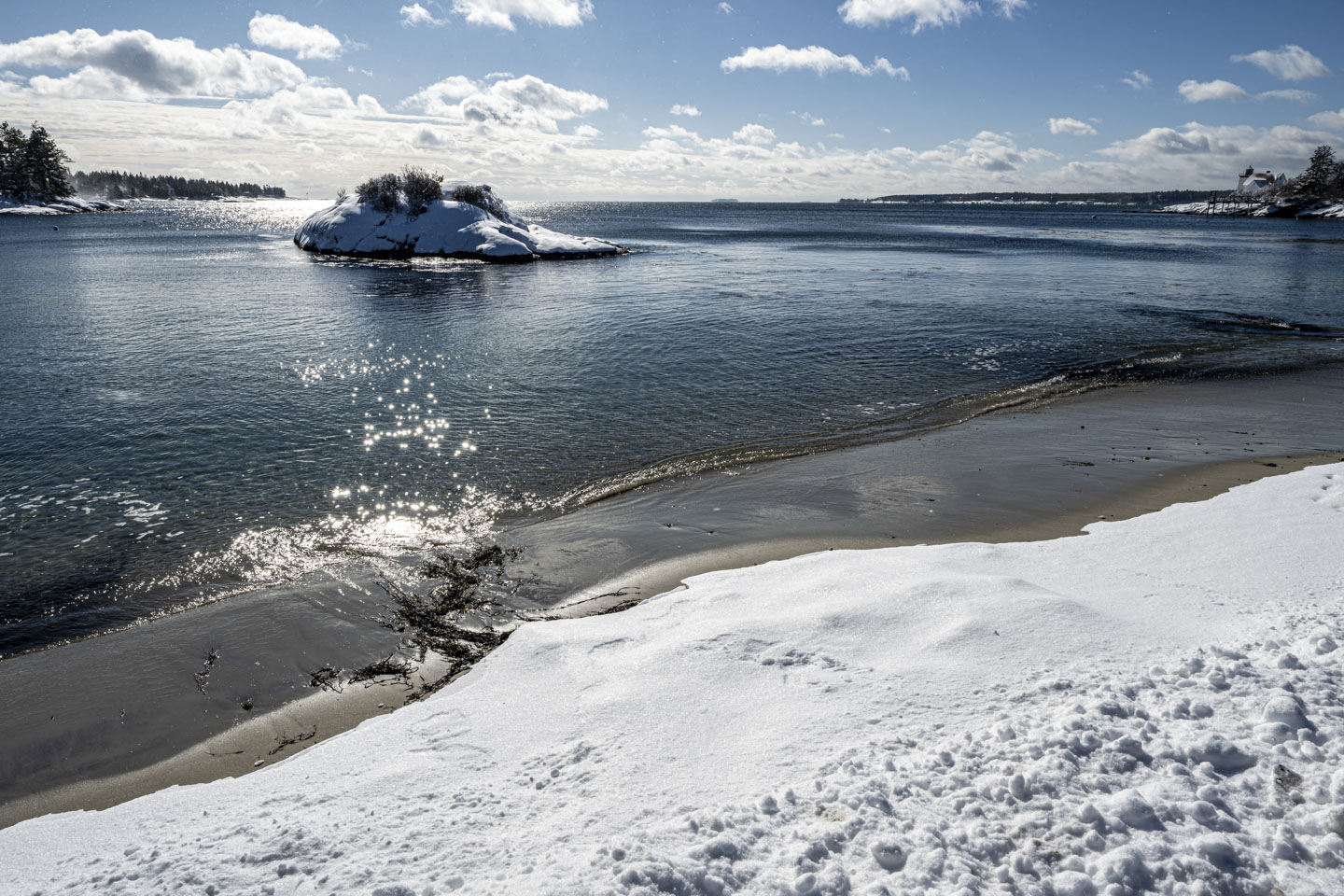 A tiny bit of beach is showing between snow and water, along with the snow-covered island.