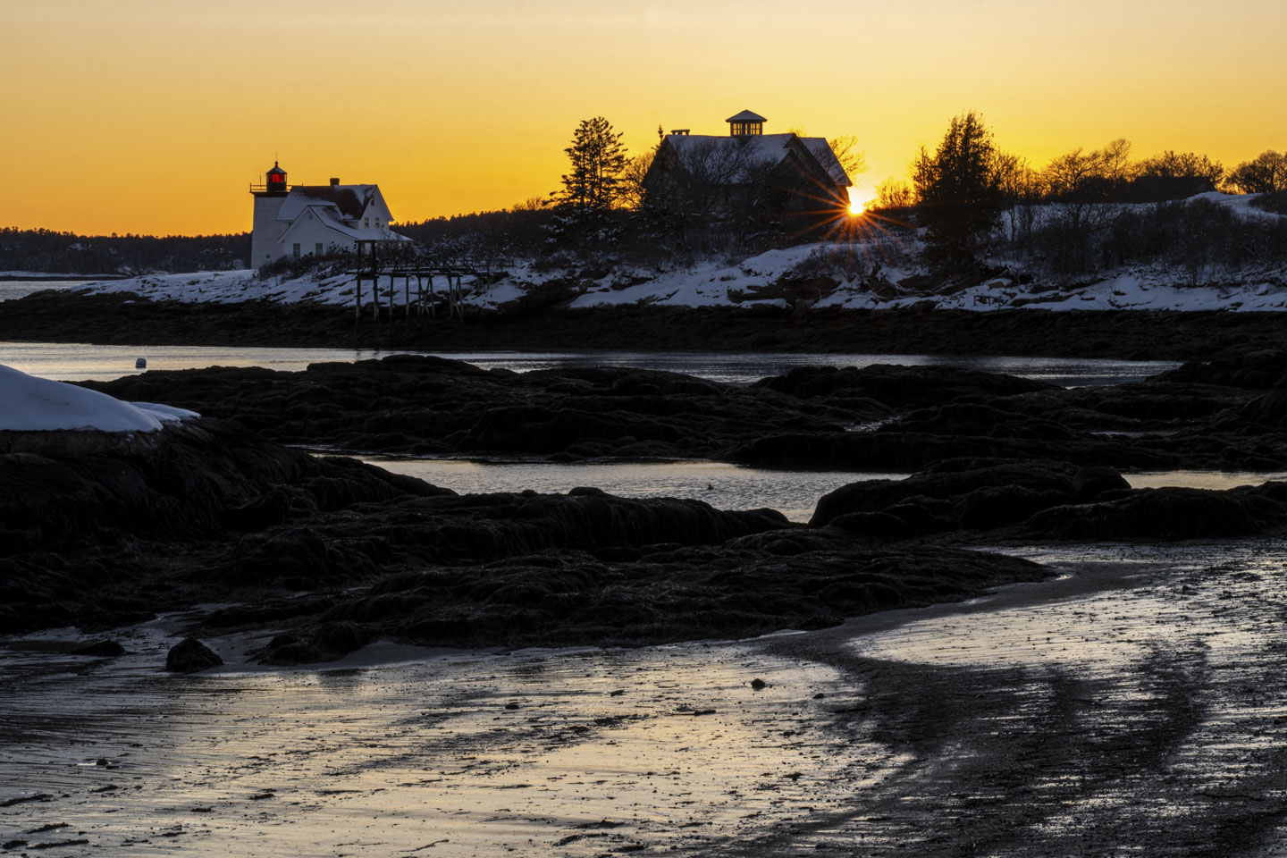 The sun is seen at the corner of a building that is next to Hendricks Head. The tide is low.