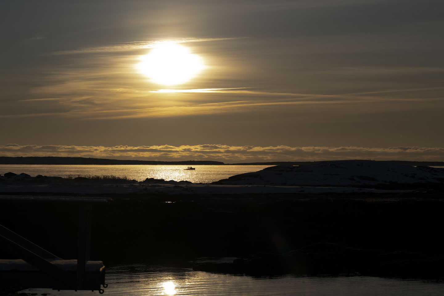 A small boat is slowly traveling through the sun trail reflected on the water.