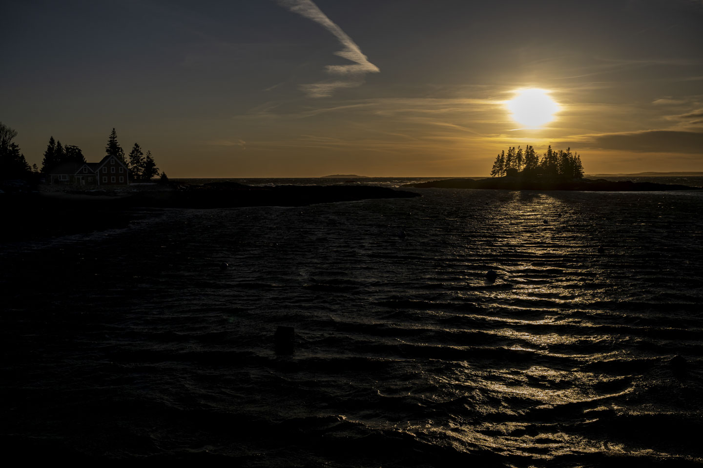 The large glow of the setting sun is behind some clouds, and an island with trees is light from behind.