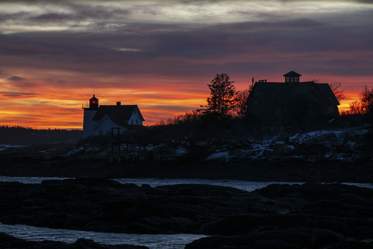 A red and orange sunset sky is behind Hendricks Head Lighthouse.