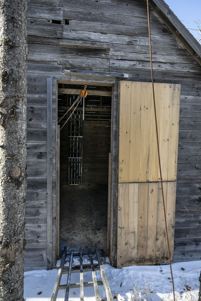 Looking into the ice barn door, which has fresh wood on it, an empty barn can be seen.