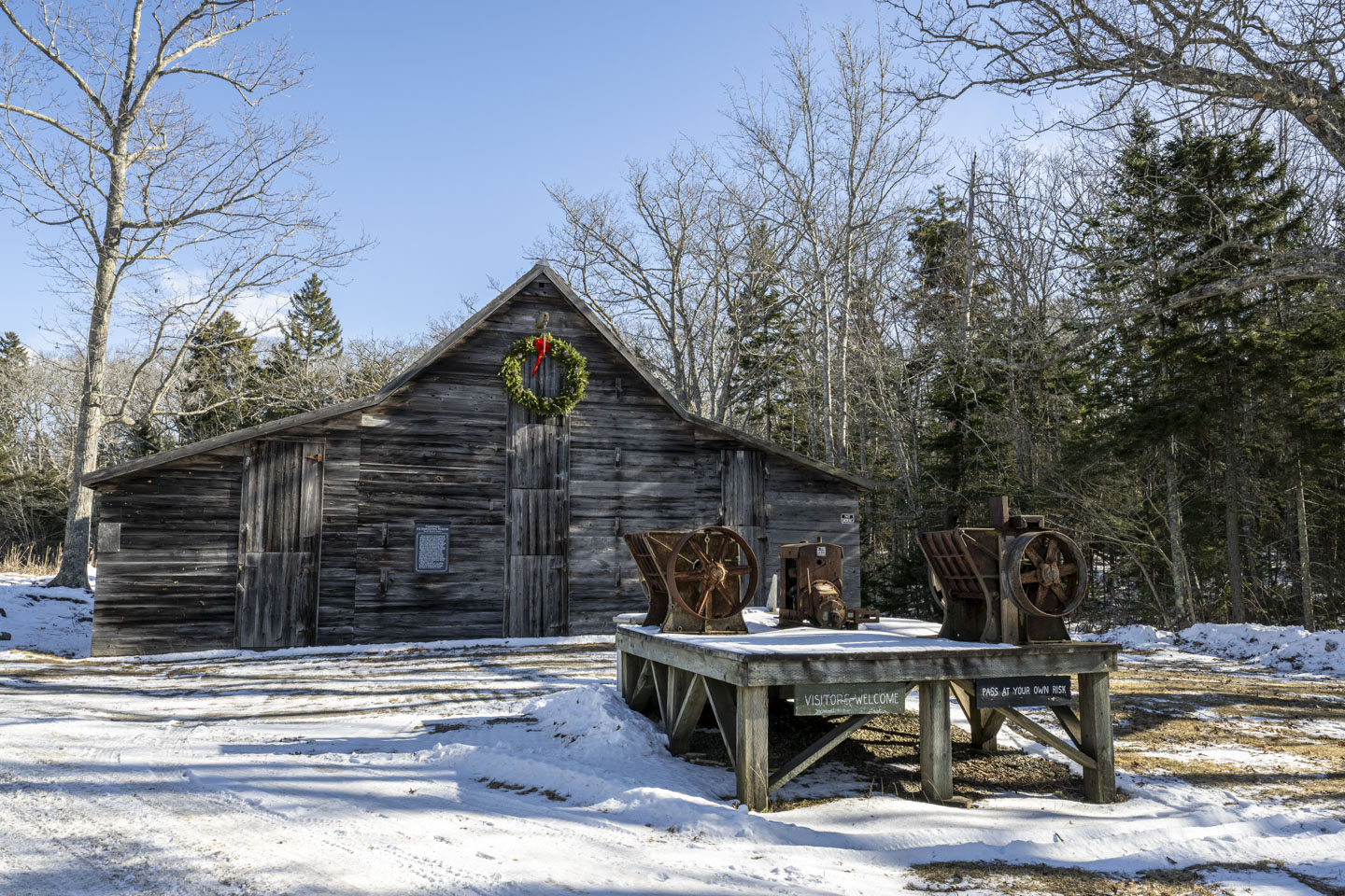 At the entrance to the Thompson Ice House, there is a platform exhibiting some old machinery. A large green wreath is hanging on the barn.