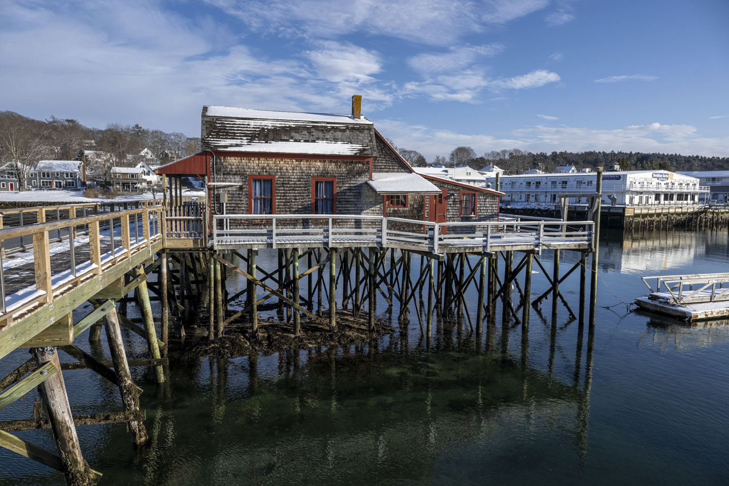 A little house is on stilts over water, with some snow on the roof.