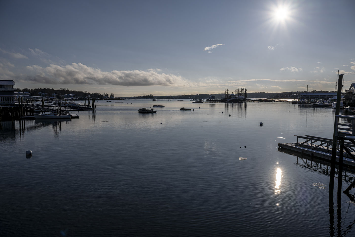 The sun is in the sky and shines on water in a harbor view.