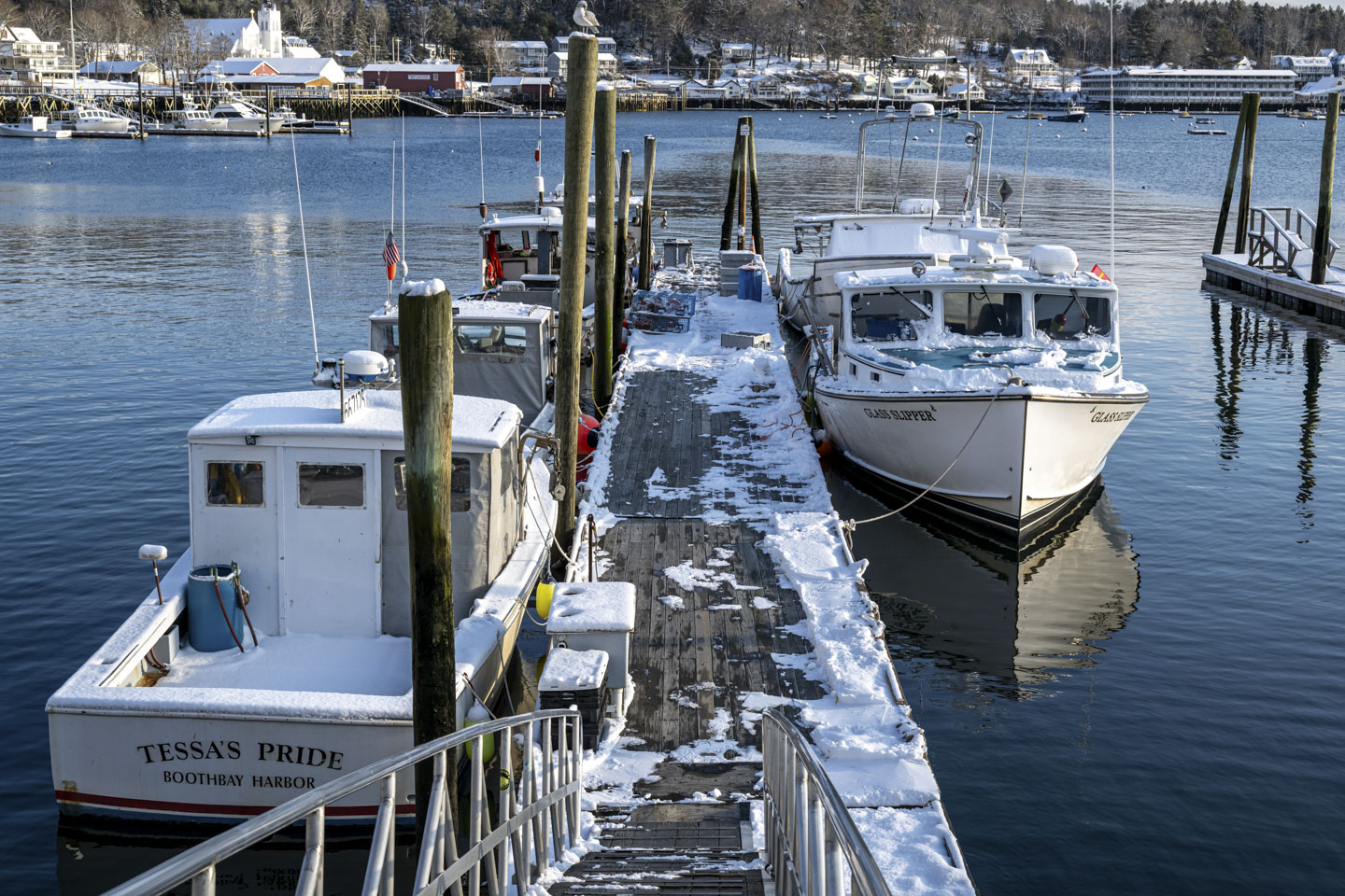 5 boats are tied up to a partially snow-covered dock.