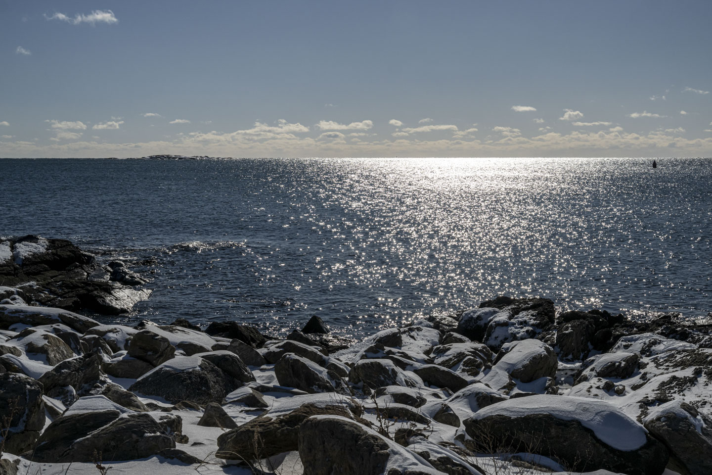 Snow covered rocks lead to a sparkling ocean.