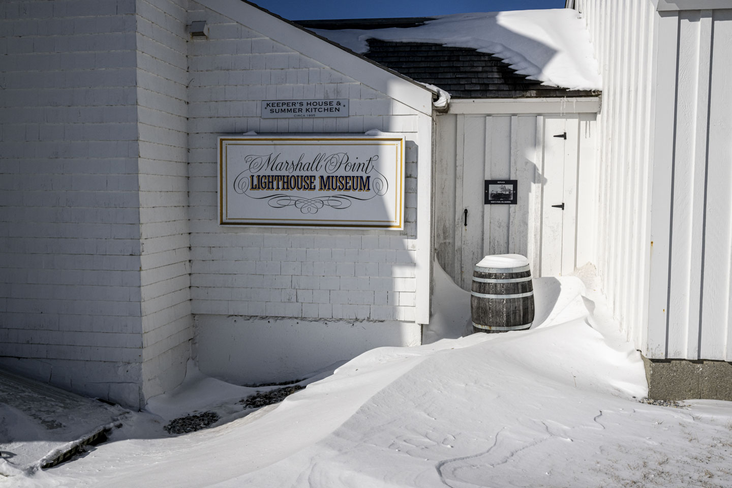 The Marshall point Lighthouse Museum sign has snow in front of it.