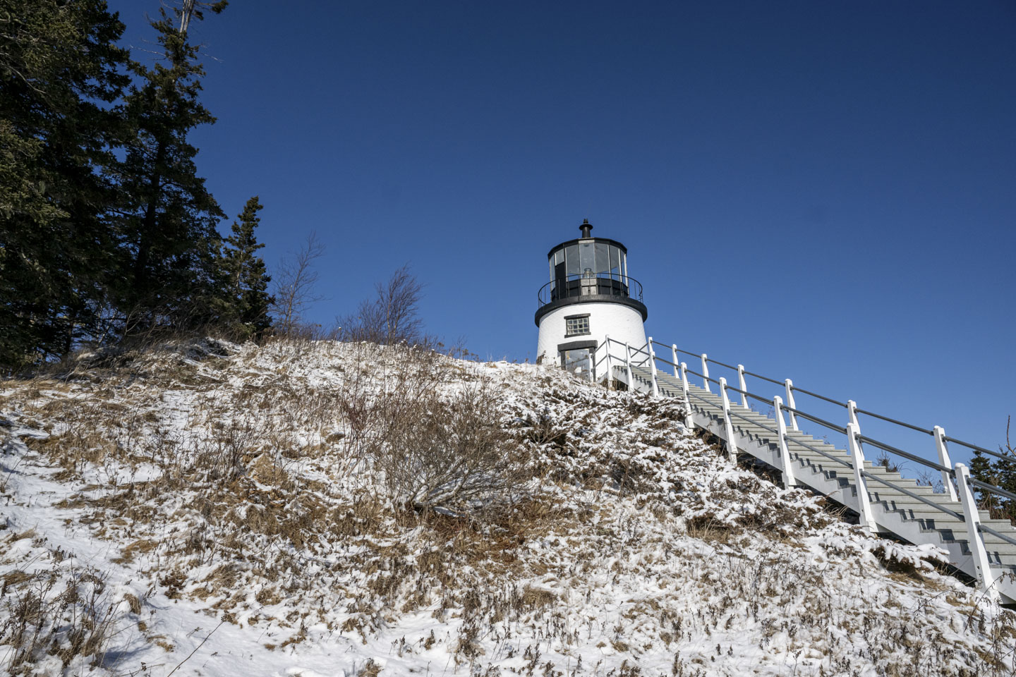 Looking up a snow-covered hill, the lighthouse is visible. There are steep steps on the right.