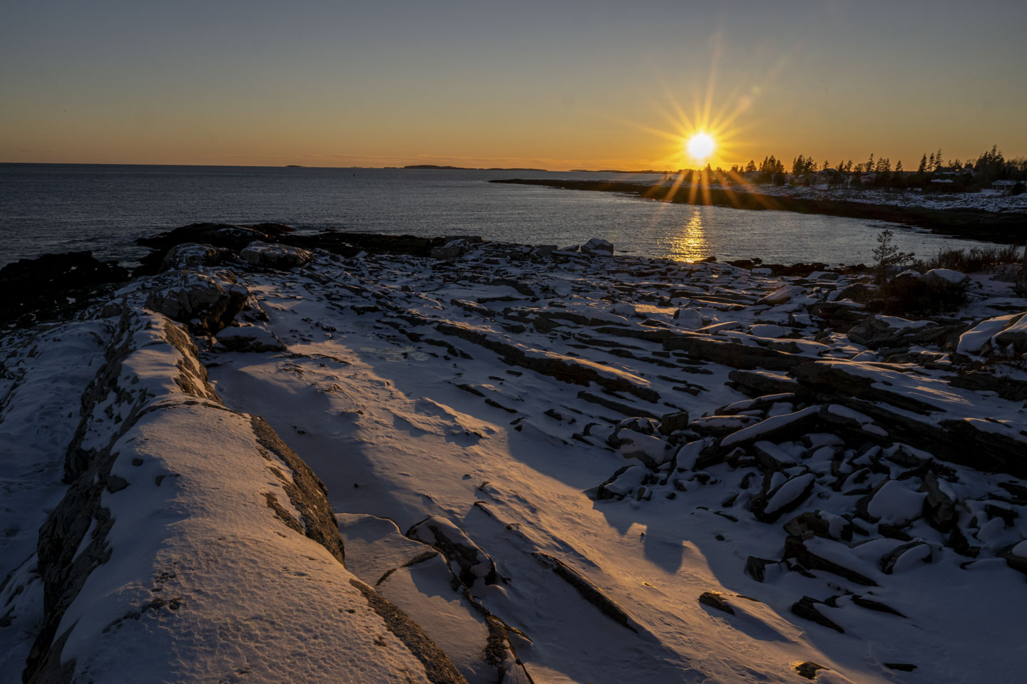 The setting sun shines over snow covered rocks.