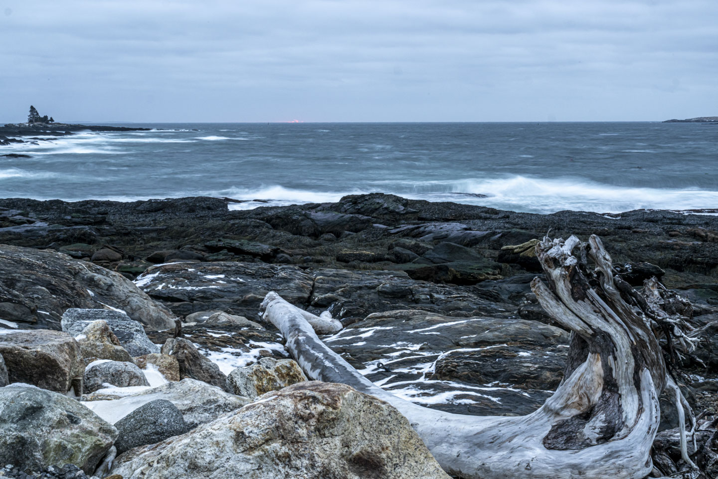Wispy waves on the ocean are between rocks and the faintest glow on the horizon.