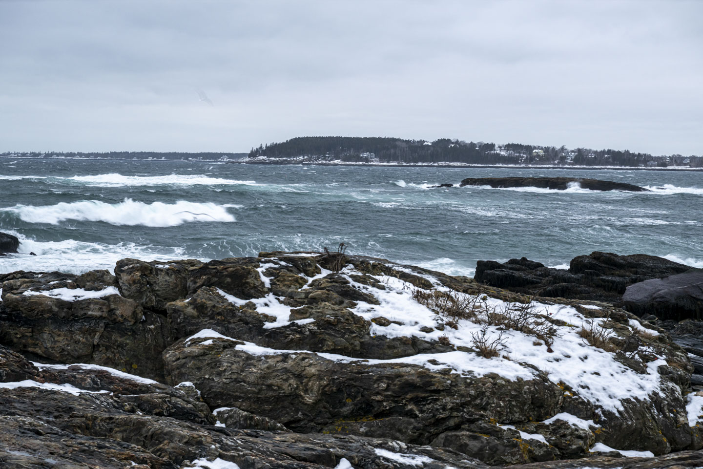 Rocks with a bit of snow are in front of water that has a lot of waves.
