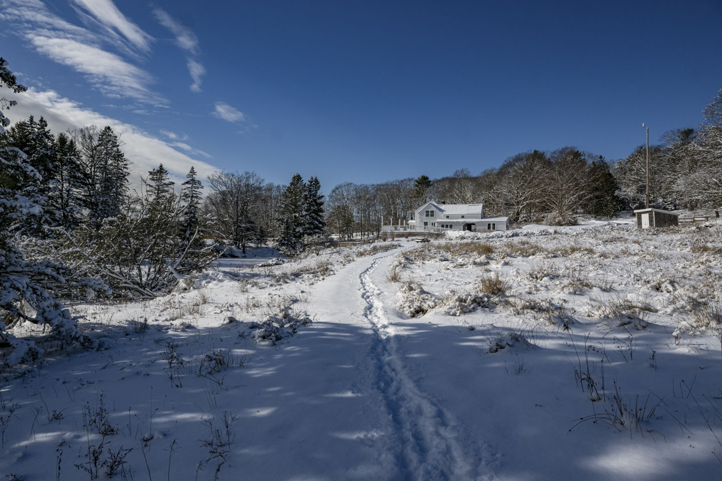A trail through the snow leads back to a large white building and a snow-covered picnic table.