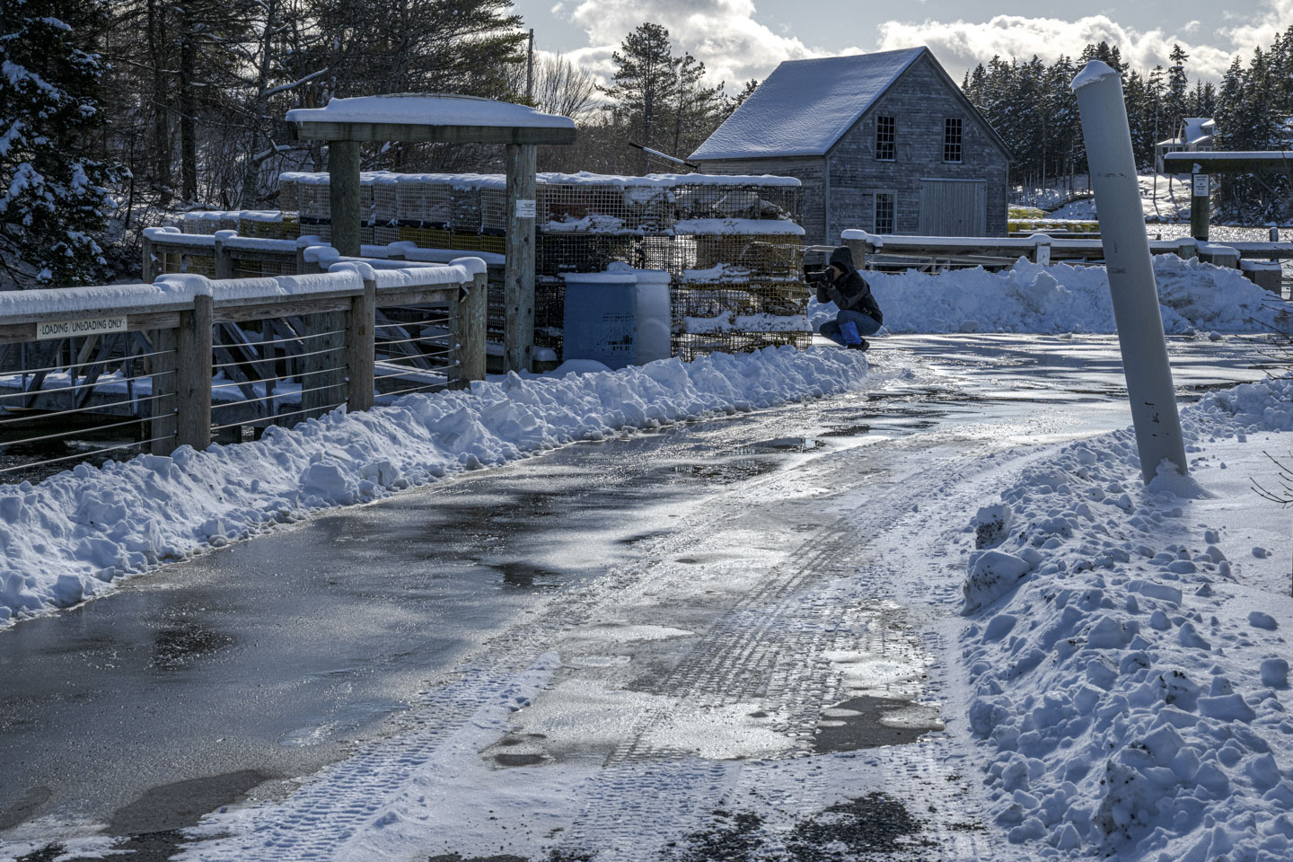 Anne is crouched on a plowed parking area, taking a picture of some lobster traps.