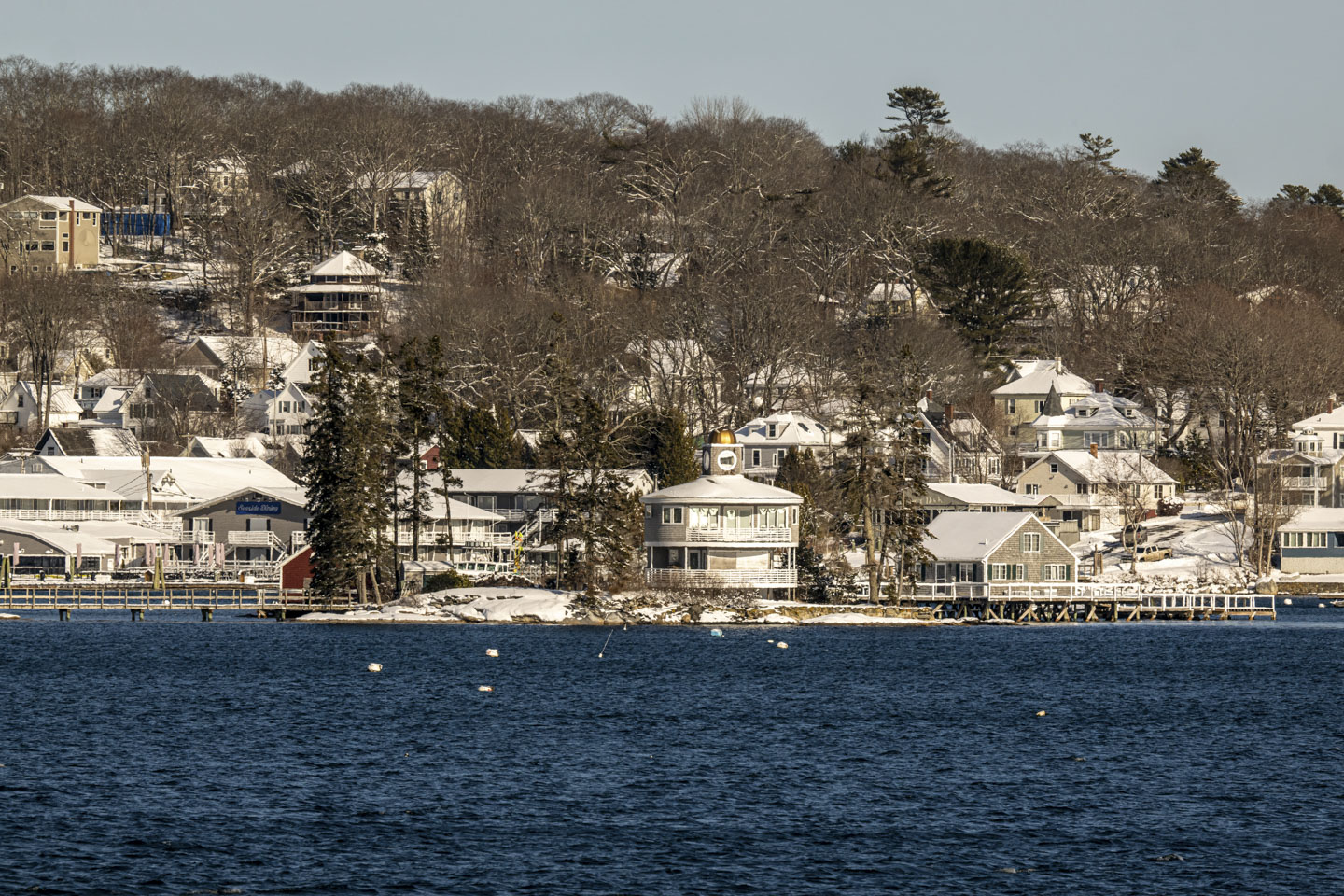 A view across the water to a round building on an island, and the mainland behind it.