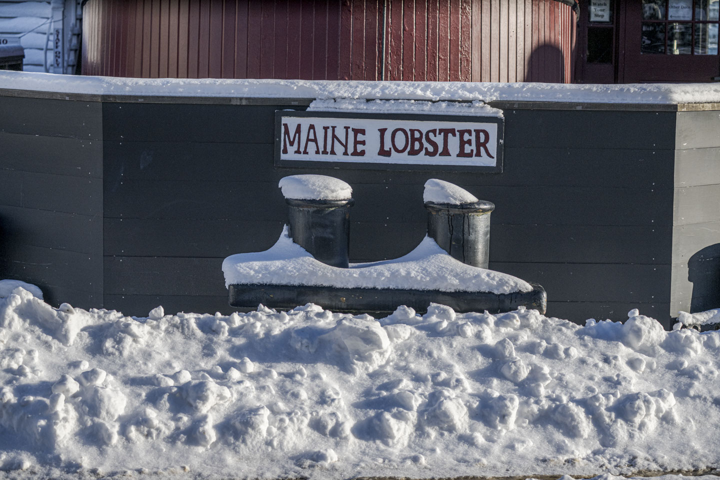 A sign that says Maine Lobster is on a black wall, with snow all around.