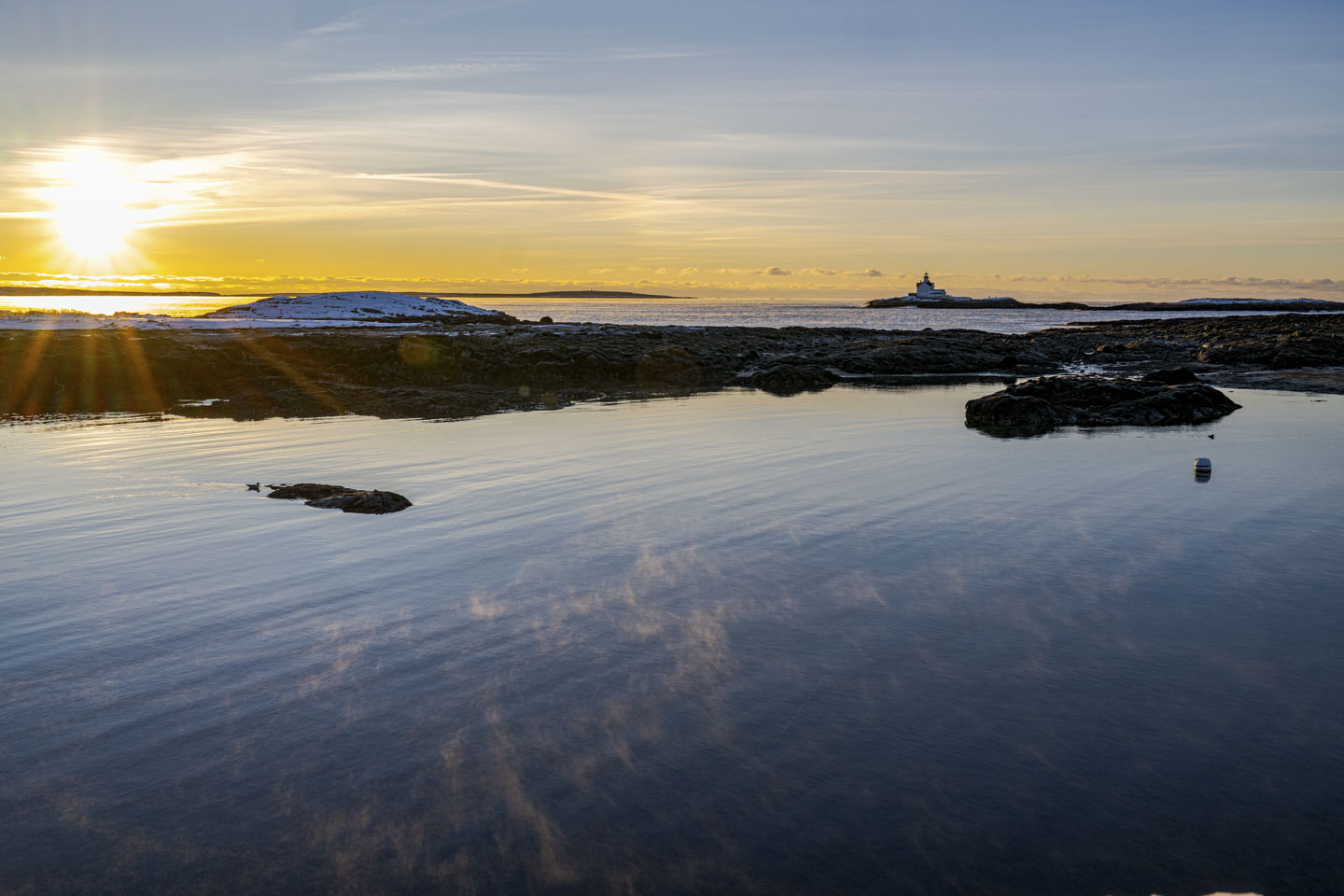 The rising sun is on the left, and Cuckold light is on the right. Nearby some sea smoke rises off of the water.