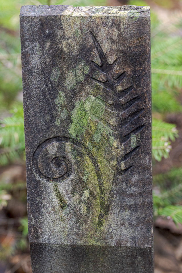 A wood signpost has a fern engraved on it.