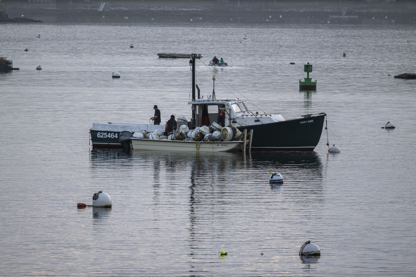 Two men are putting large buoys from a medium sized boat into a small boat.