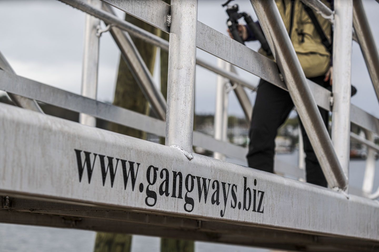 The metal gangway from the footbridge to the dock, with a person partially seen walking on it.