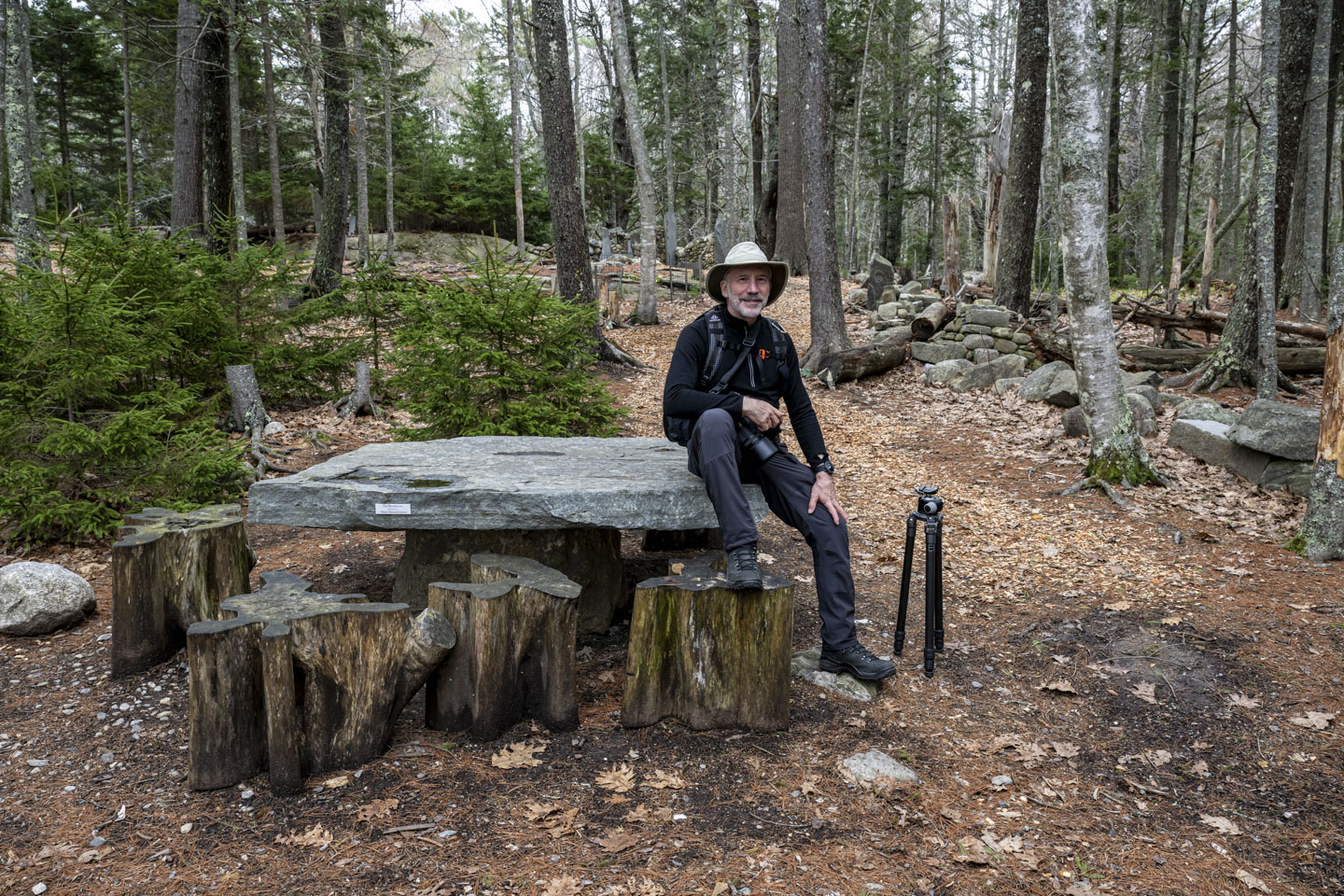 Paul is sitting on a stone table in the woods.