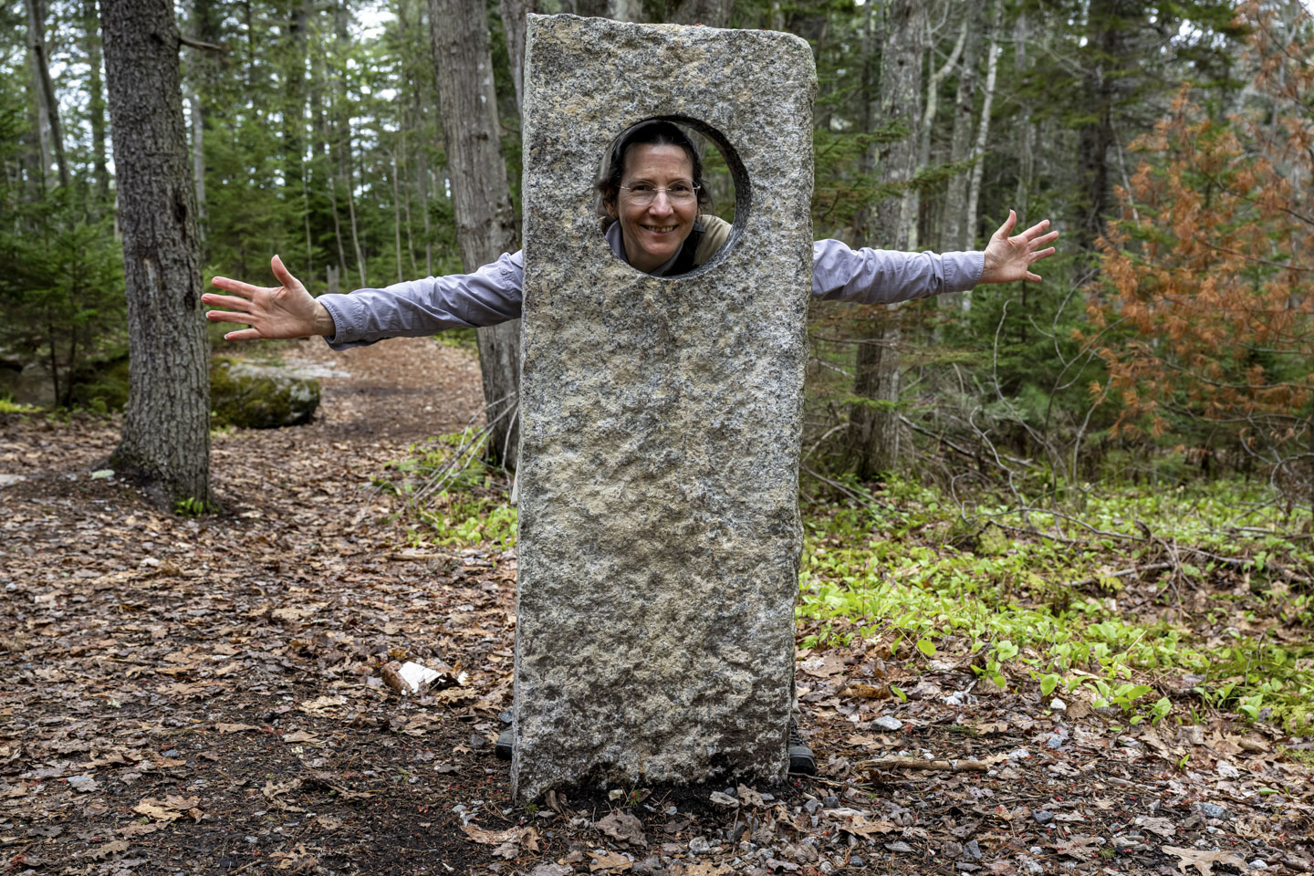 Anne is looking through a stone post with a large hole, holding her arms out to the sides.