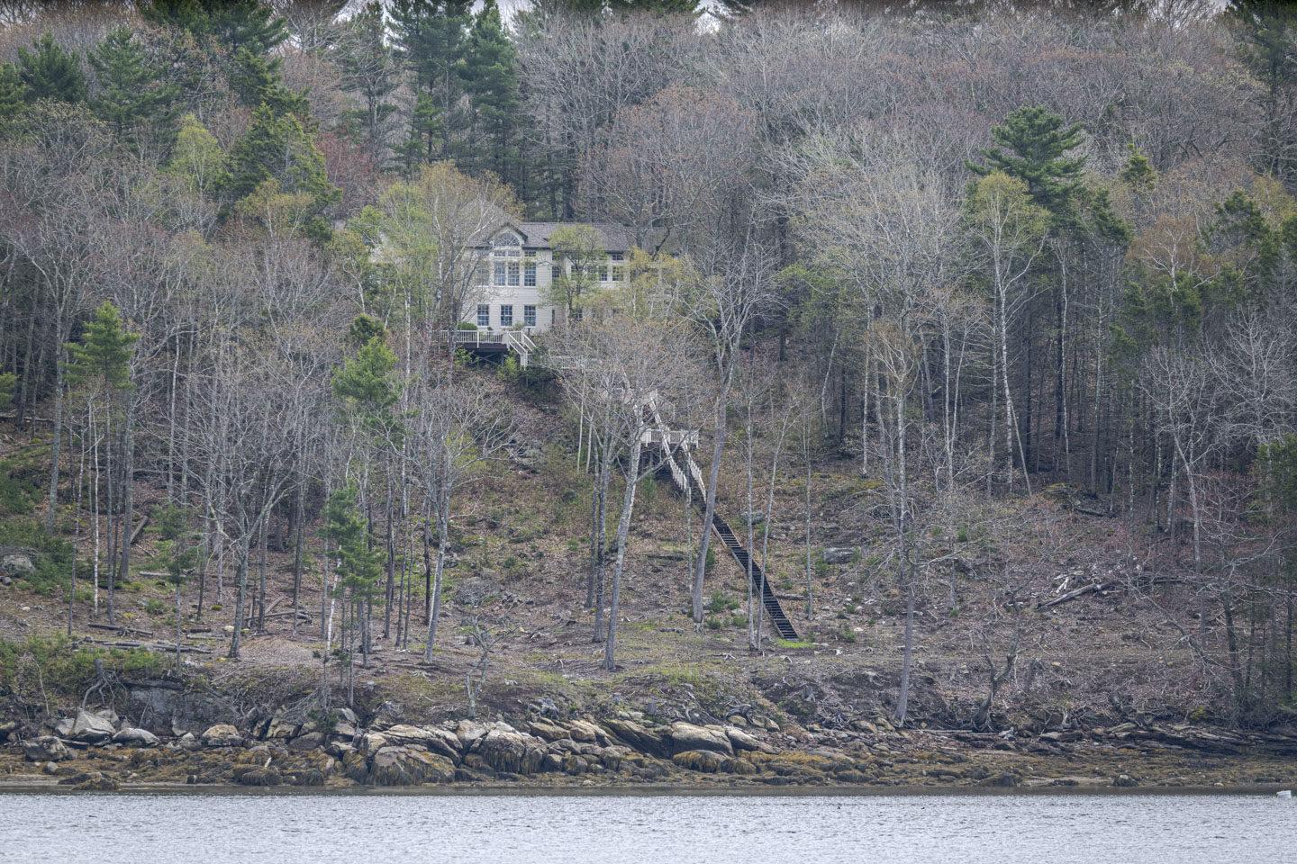 A large house sits on a hill on the riverbank, with a long and steep set of stairs leading to is.