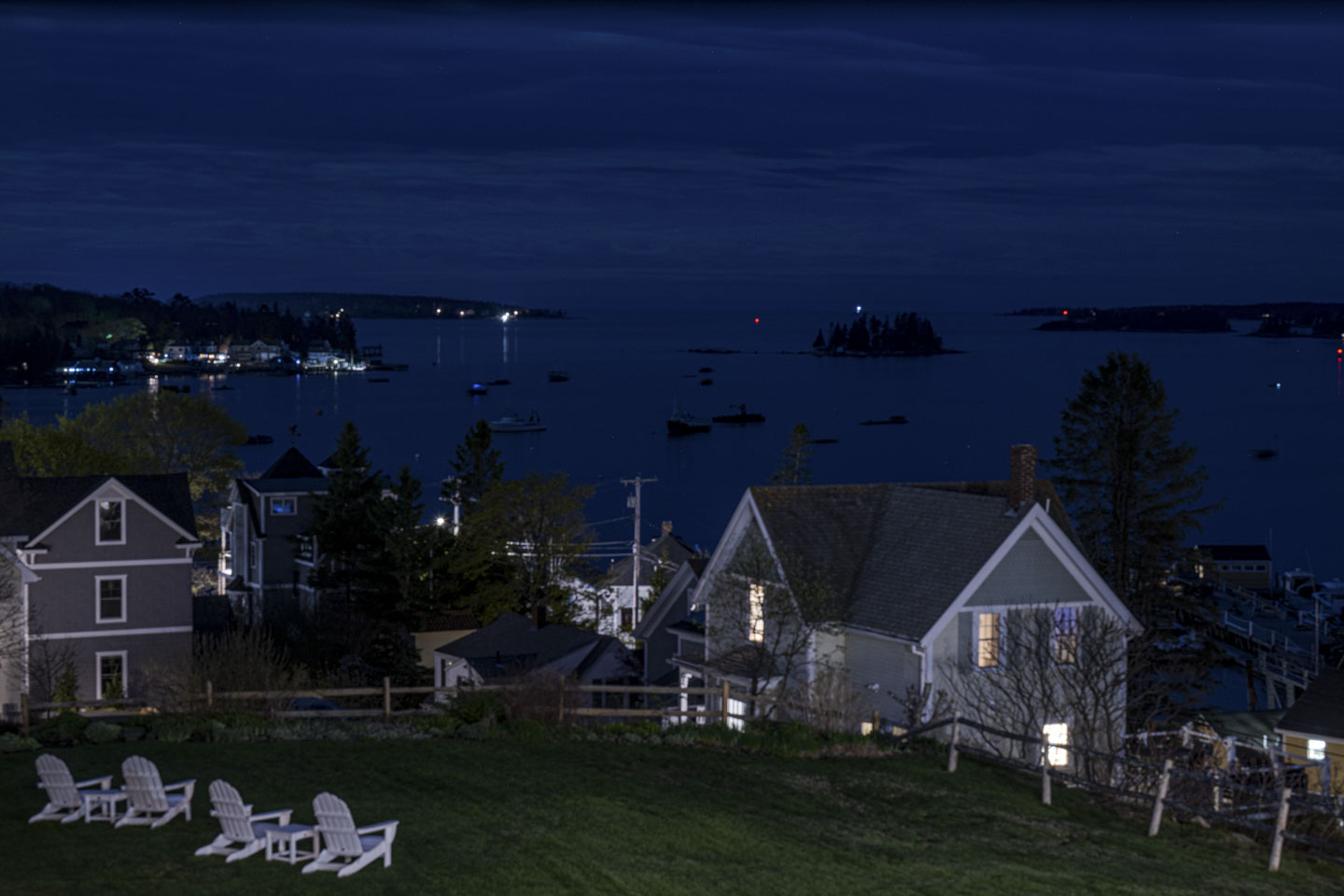 A night view across the lawn and to Boothbay Harbor with lights visible in the houses and on the water.