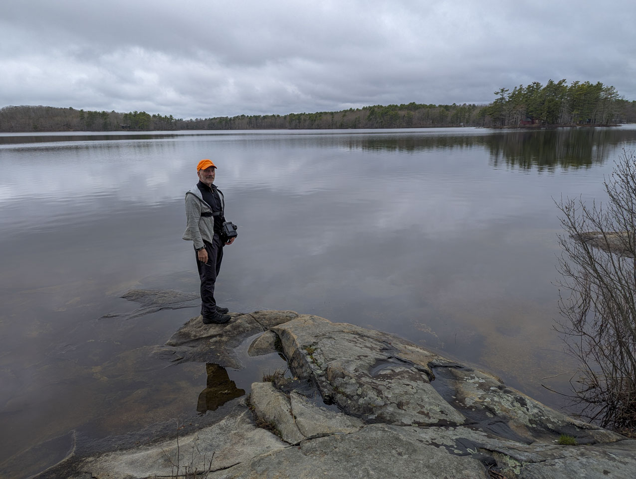Paul is standing at the end of a rock formation on the edge of a pond.